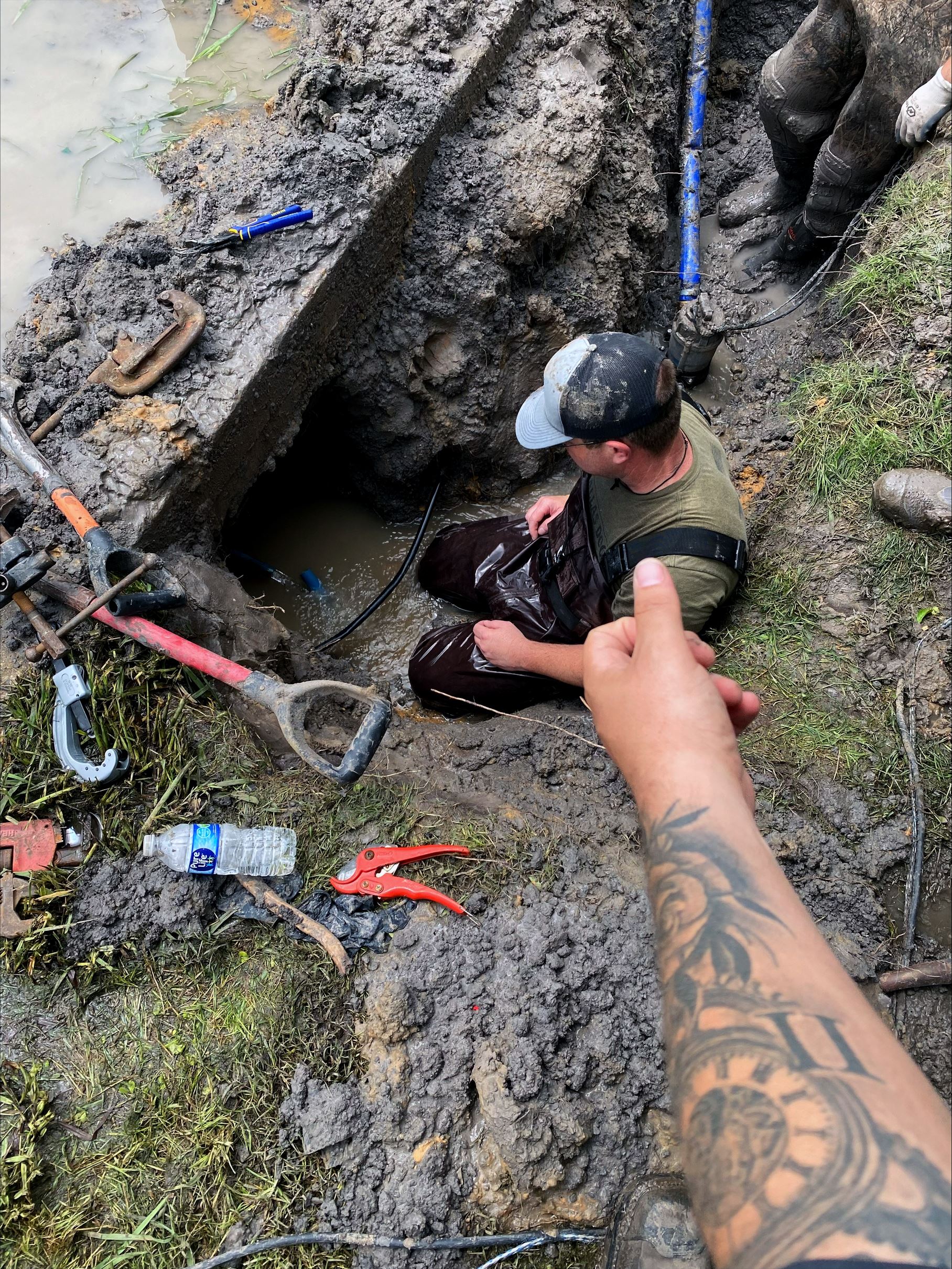 Public Works employee in a water logged hole looking at a pipe